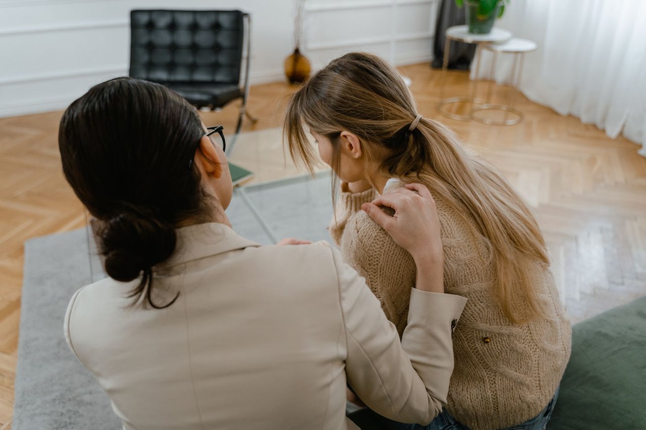 Duas mulheres sentadas em ambiente interno, conversando com expressão de empatia e apoio mútuo.