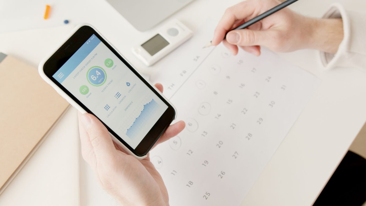 Mãos usam um smartphone para acompanhar indicadores de saúde enquanto planejam atividades em um calendário.